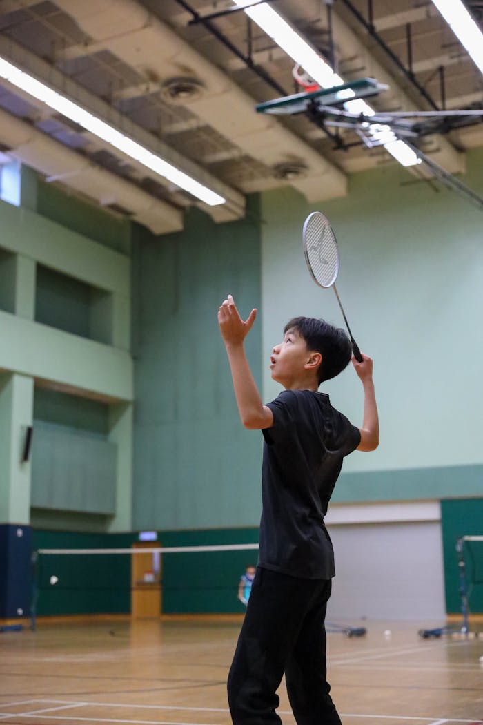 A young boy playing badminton in an indoor gym, focusing on the shuttlecock.