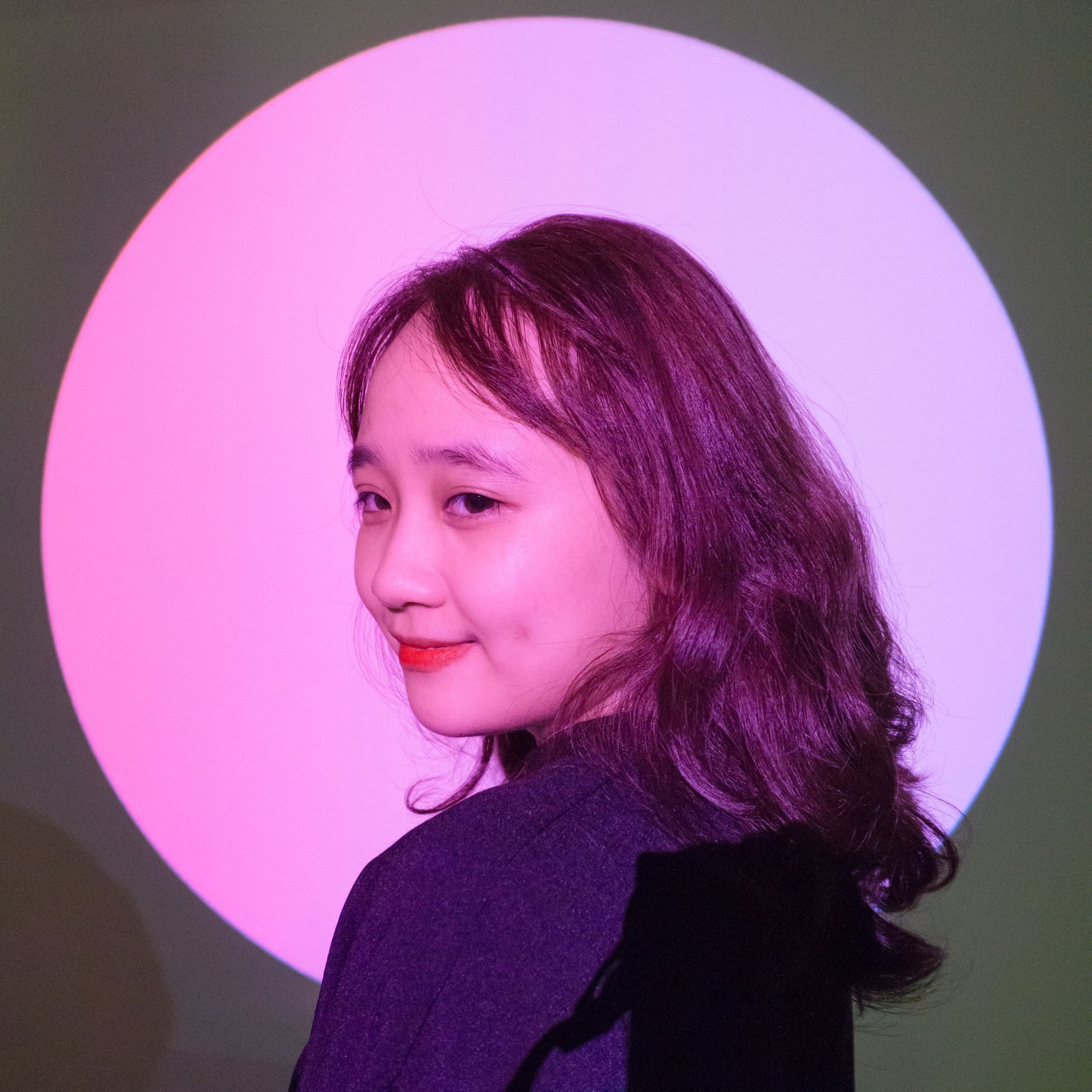 Artistic portrait of a woman posed in a vibrant pink and green spotlight with a playful demeanor.