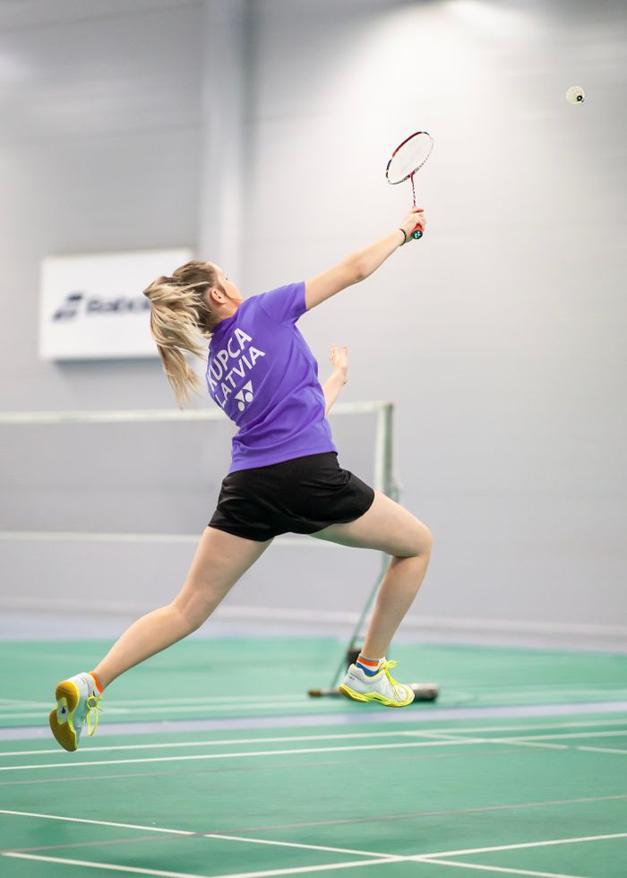Dynamic action shot of a woman playing badminton indoors, showcasing athletic skill.