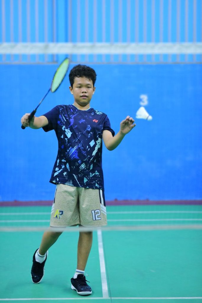A young boy plays badminton on an indoor court wearing sports attire.